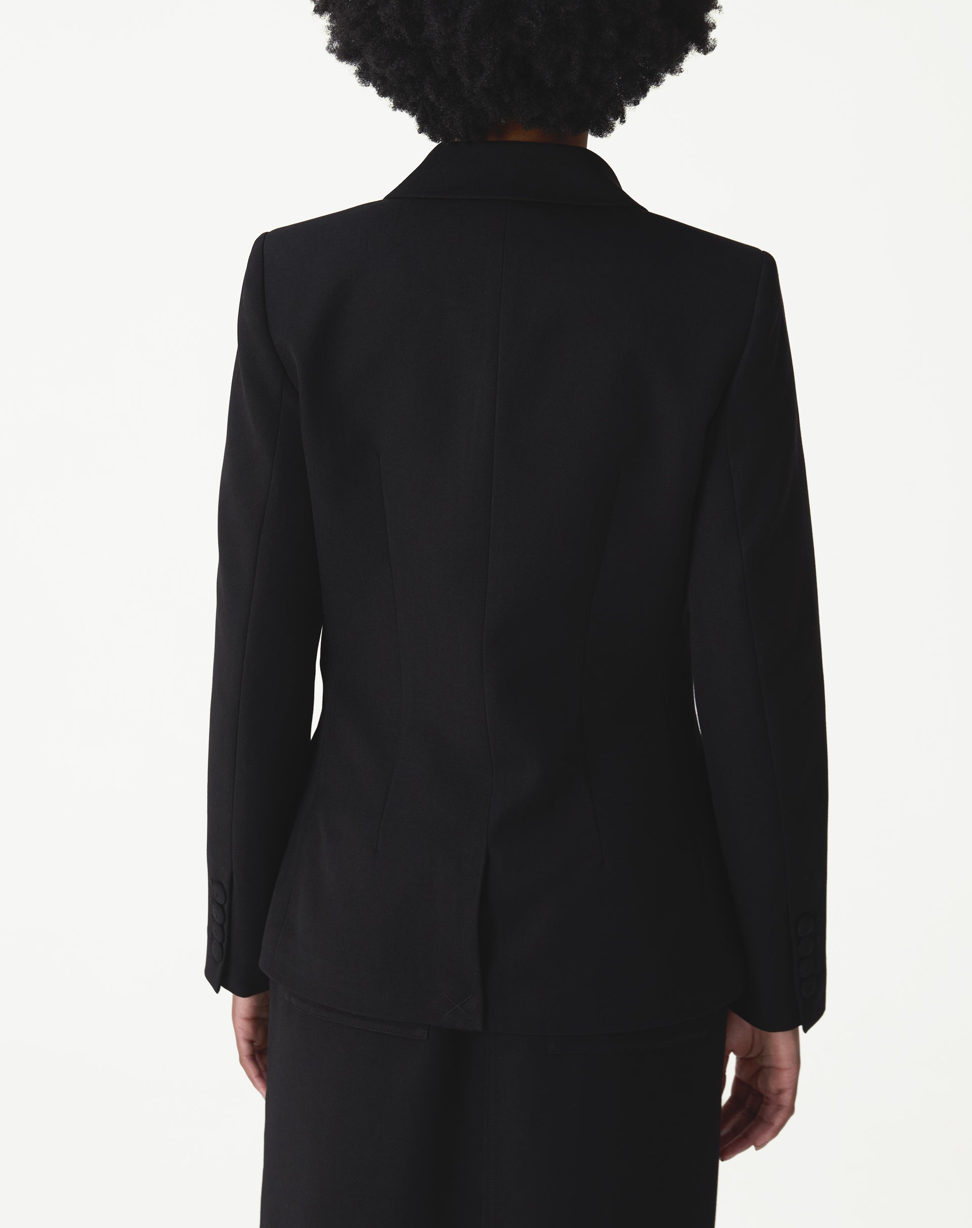 Vista traseira do blazer preto longo em modelo, com costura central e fenda única