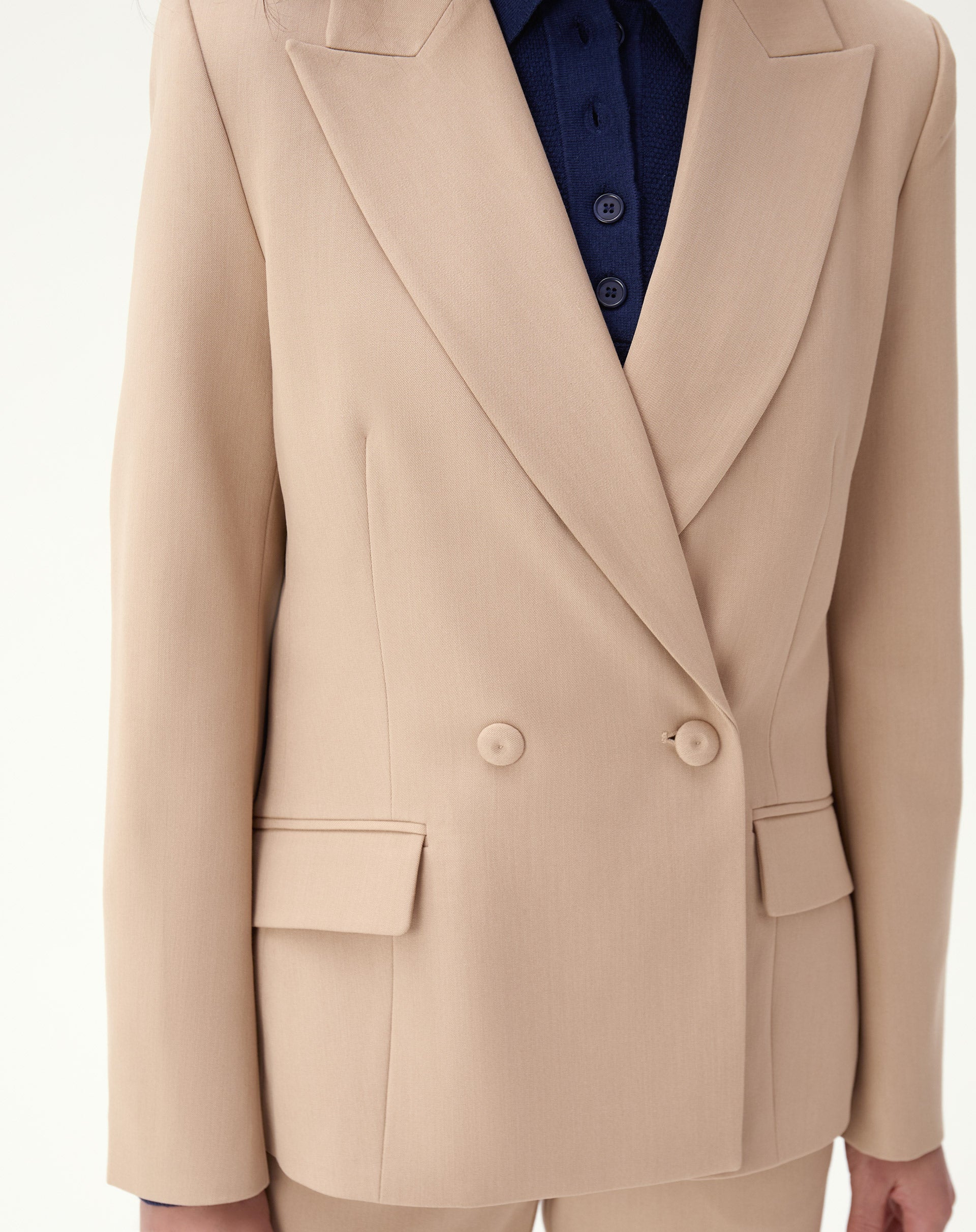 Close detalhado do blazer bege exibindo lapelas pontiagudas e abotoamento frontal.