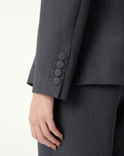 Detalhe frontal do blazer cinza: botões revestidos e bolso com aba, costura e textura do tecido