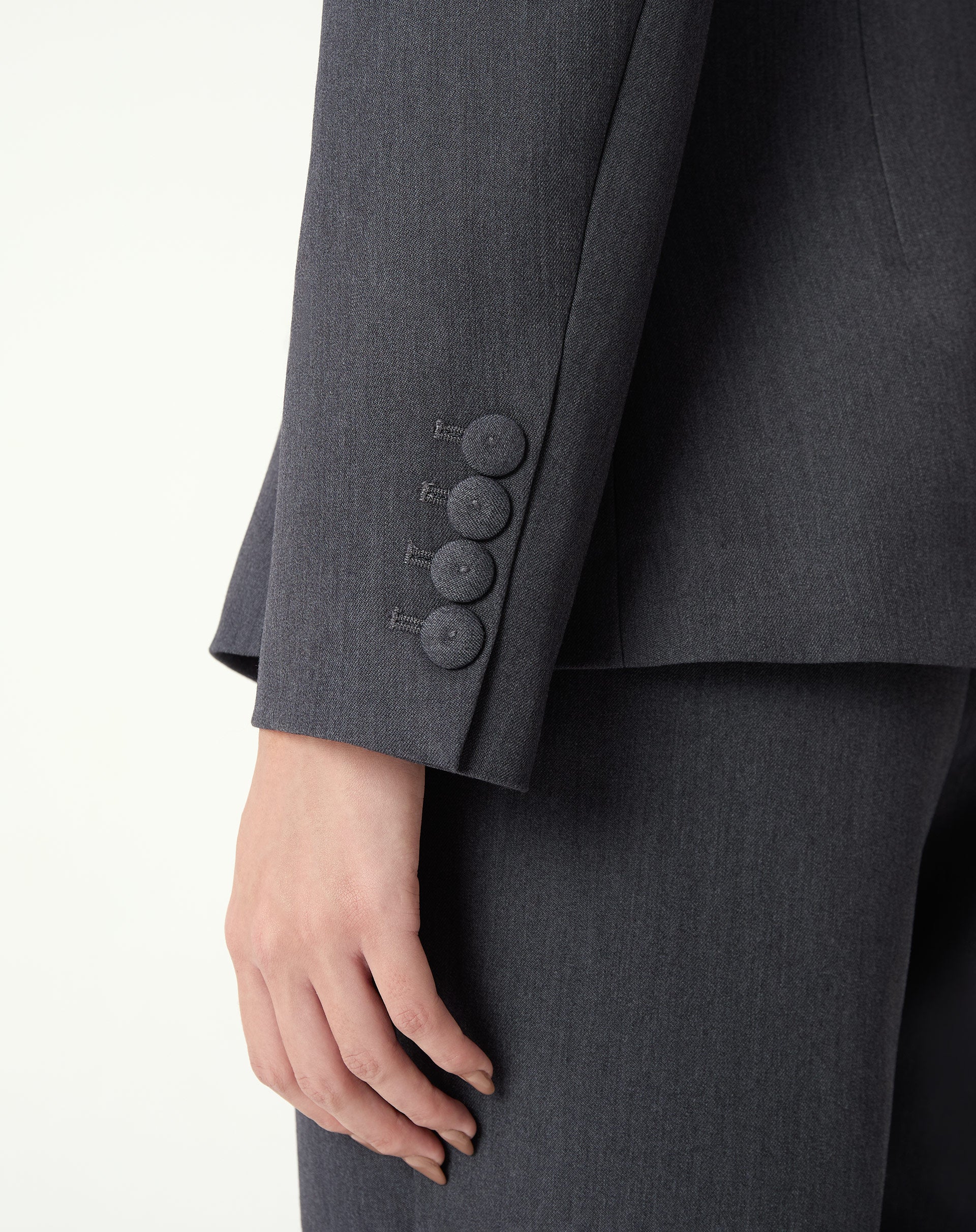 Detalhe frontal do blazer cinza: botões revestidos e bolso com aba, costura e textura do tecido