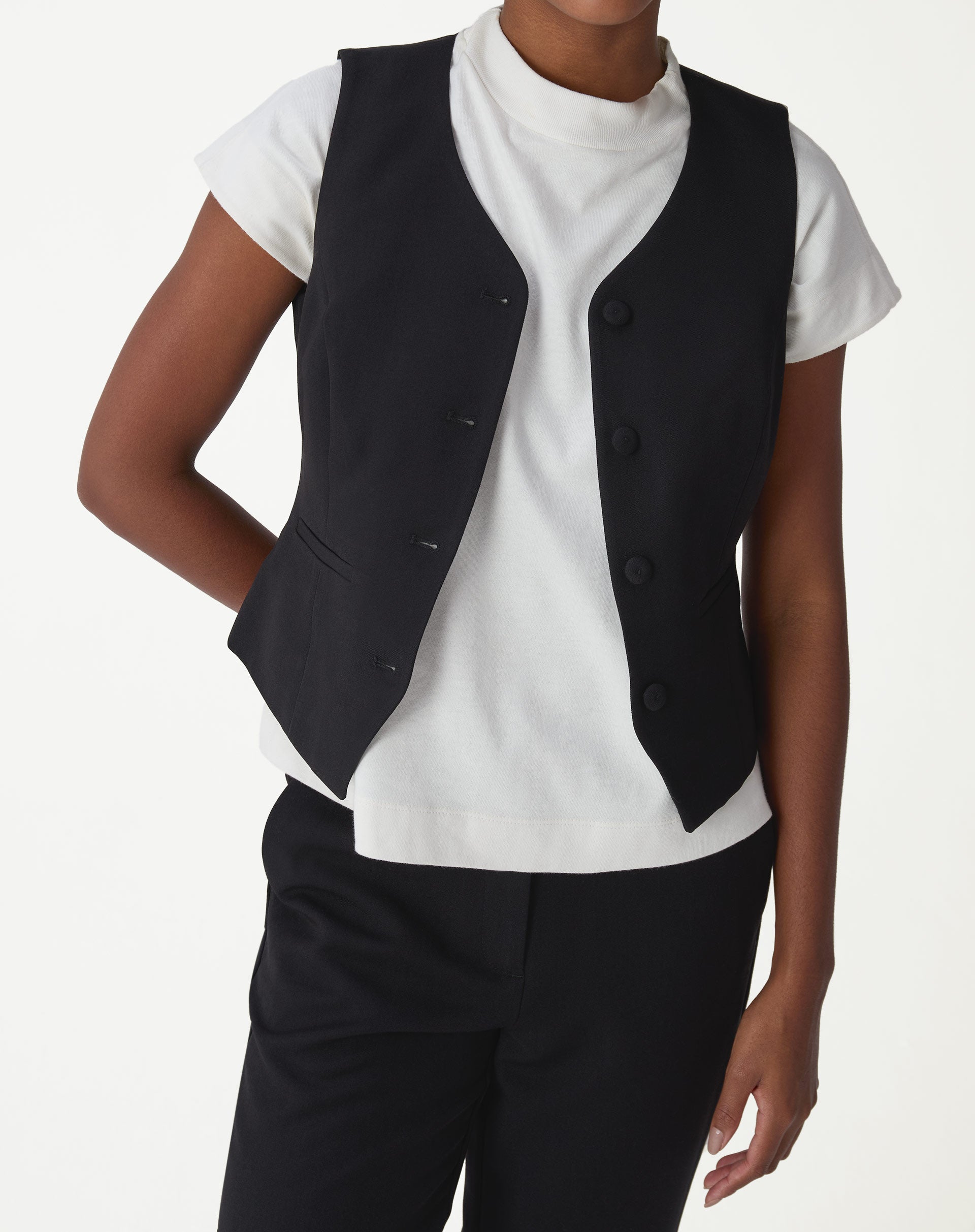 Colete alfaiataria slim preto sem mangas com botões forrados, close frontal mostrando bolsos passpa e caimento ajustado.
