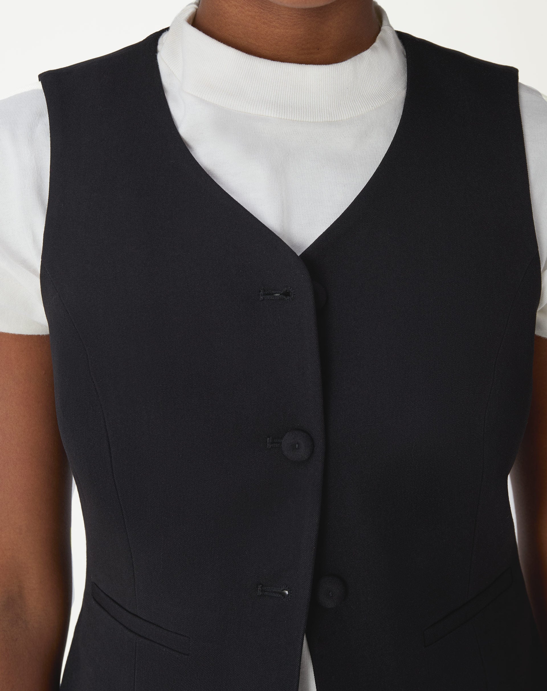 Detalhe do decote em V do colete alfaiataria preto, mostrando acabamento do bordo e forro interno.