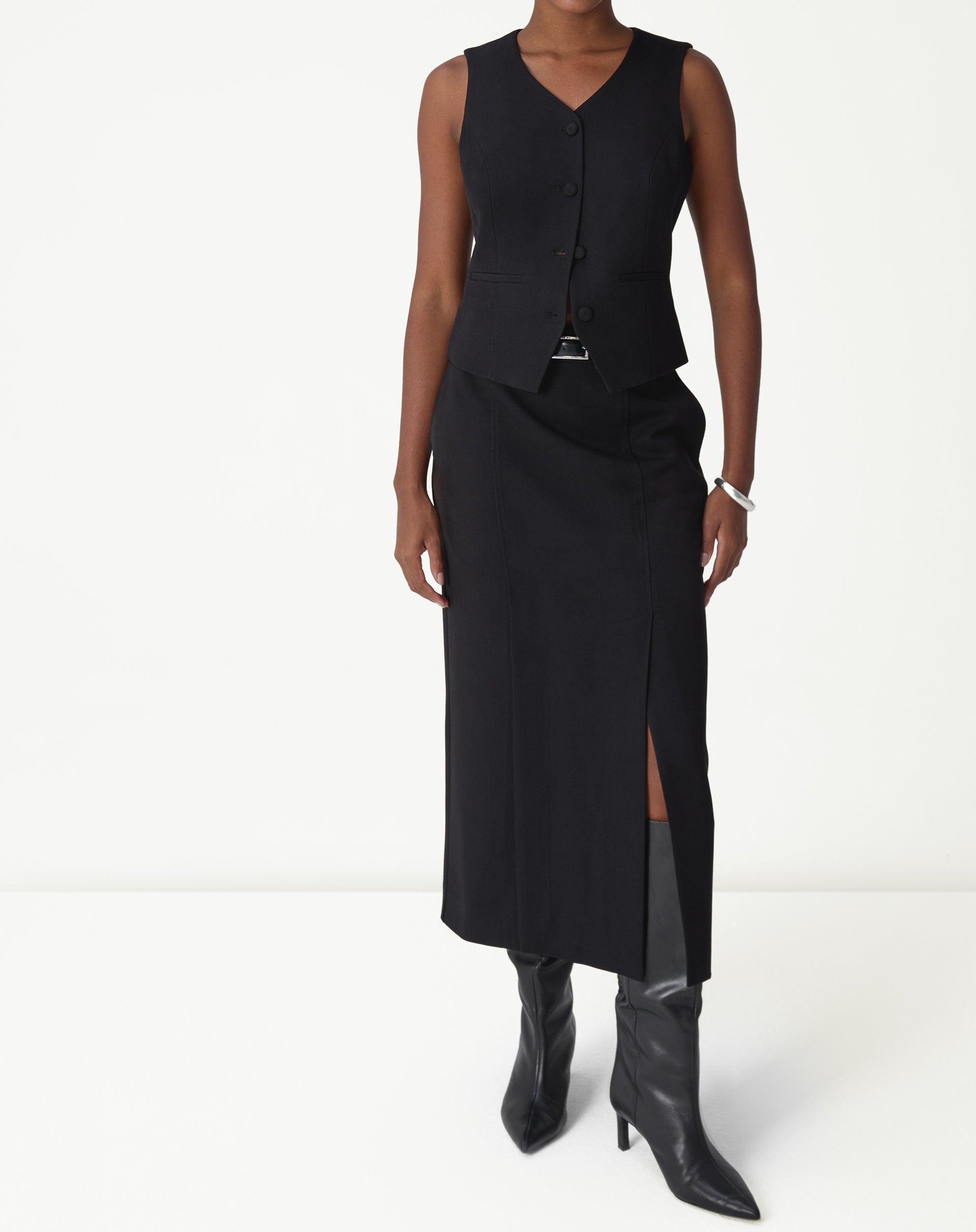 Saia midi preta alfaiataria vista frontal em modelo, corte reto com fenda lateral discreta e colete combinando.