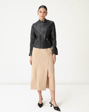 Modelo em pé vestindo saia midi alfaiataria bege com fenda frontal e cós médio, styling com jaqueta preta e sapatos pretos, vista frontal completa