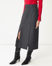 Vista lateral da saia midi cinza em modelo, evidenciando a fenda alta e o movimento da peça ao caminhar com bota preta.