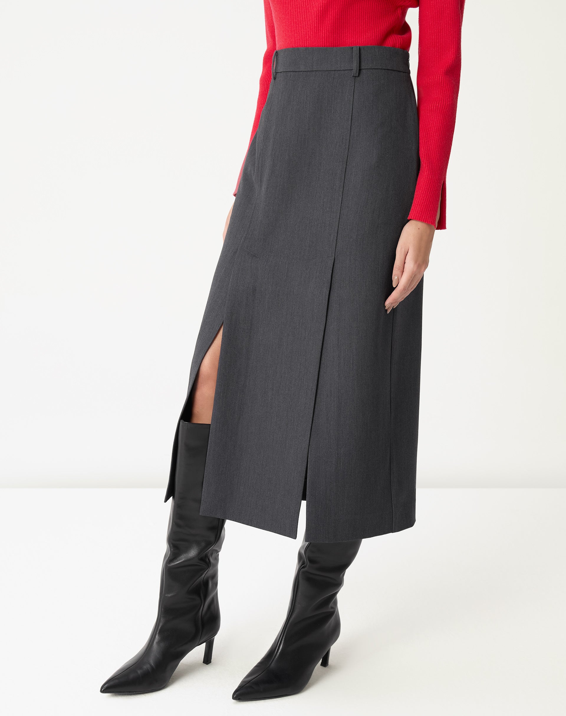 Vista lateral da saia midi cinza em modelo, evidenciando a fenda alta e o movimento da peça ao caminhar com bota preta.