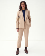 Mulher vestindo conjunto de alfaiataria bege com blazer e calça slim alfaiataria bege, look formal com blusa azul-marinho e sapatos marrons.