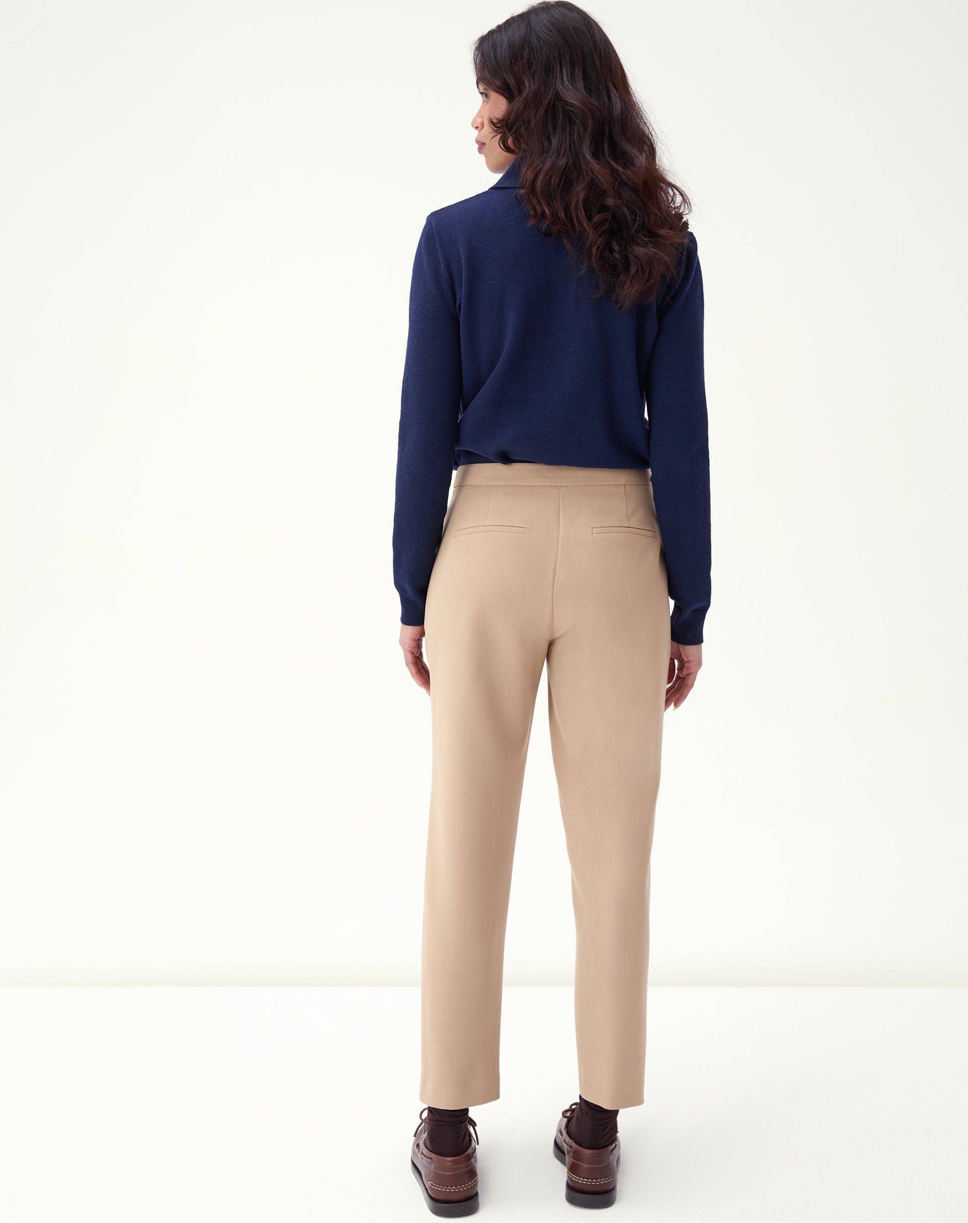 Vista posterior da calça slim alfaiataria bege em modelo, revelando caimento e acabamento refinado.