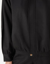 Modelo usando casaco preto com punhos largos e barra elástica, look completo com shorts pretos e mocassim - caimento estruturado