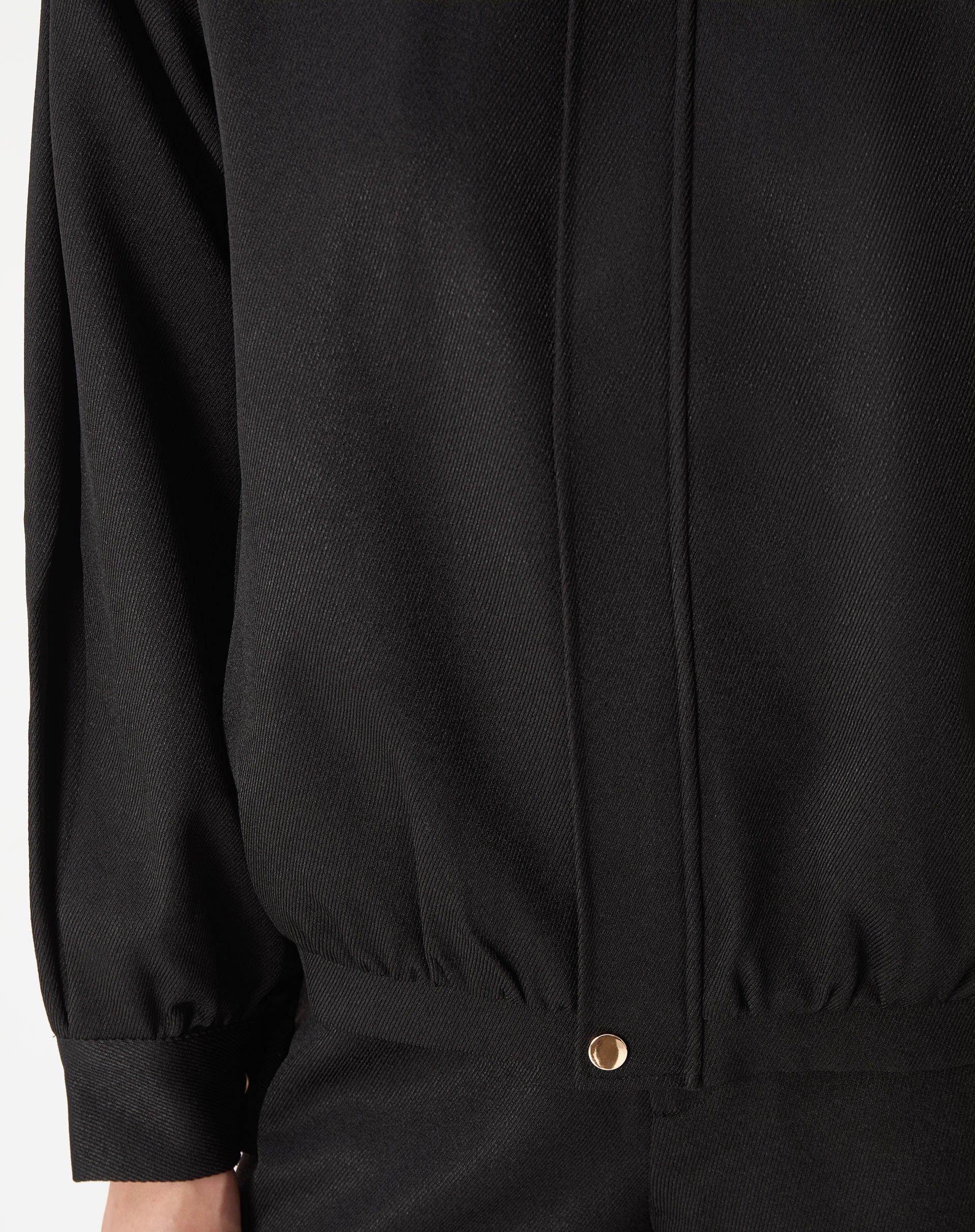 Modelo usando casaco preto com punhos largos e barra elástica, look completo com shorts pretos e mocassim - caimento estruturado