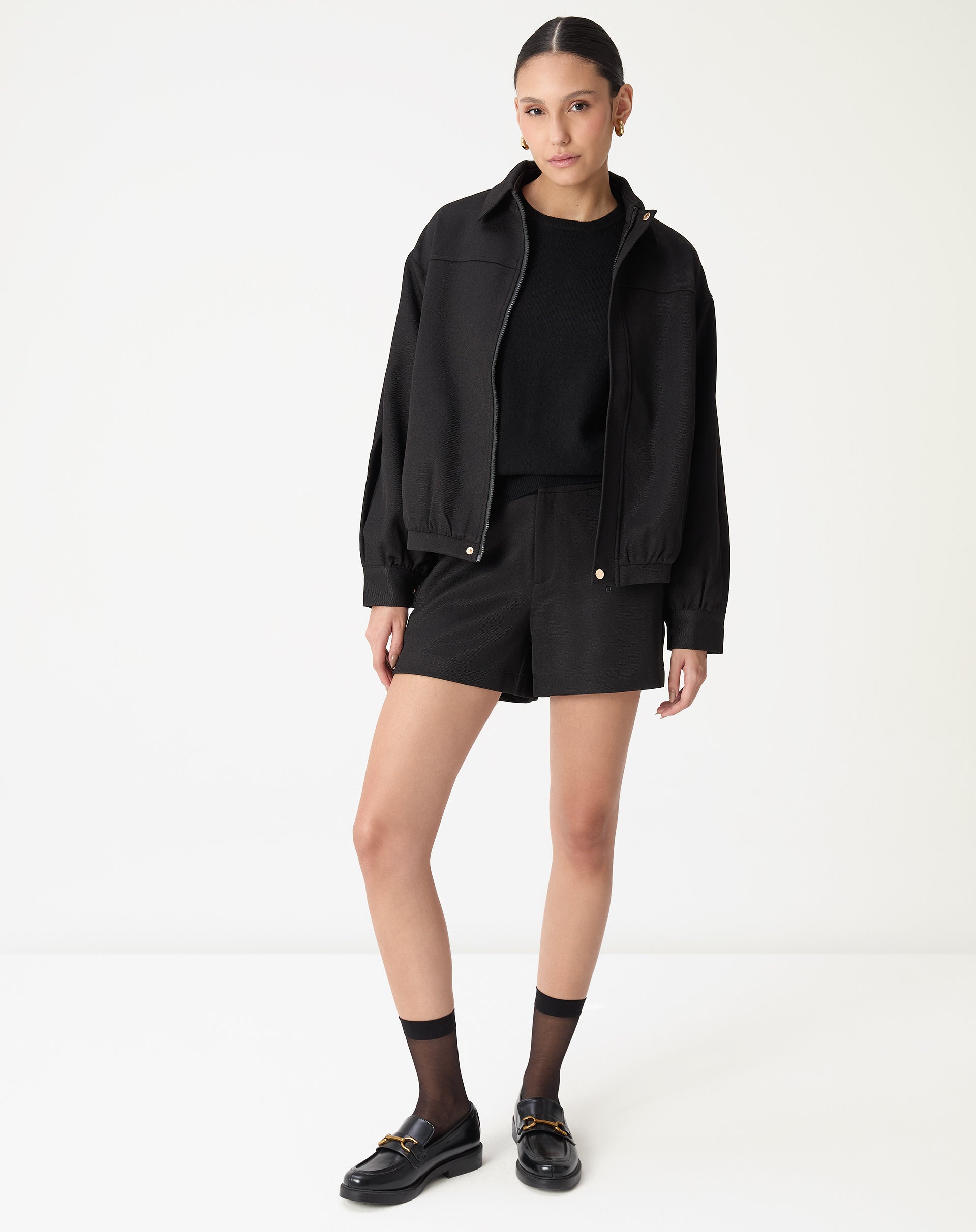 Close frontal do cós do shorts preto com passantes para cinto, pala limpa e bolso lateral discreto, detalhe de costura