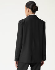 Vista traseira do blazer oversized preto mostrando costura central e fenda única, caimento alongado.