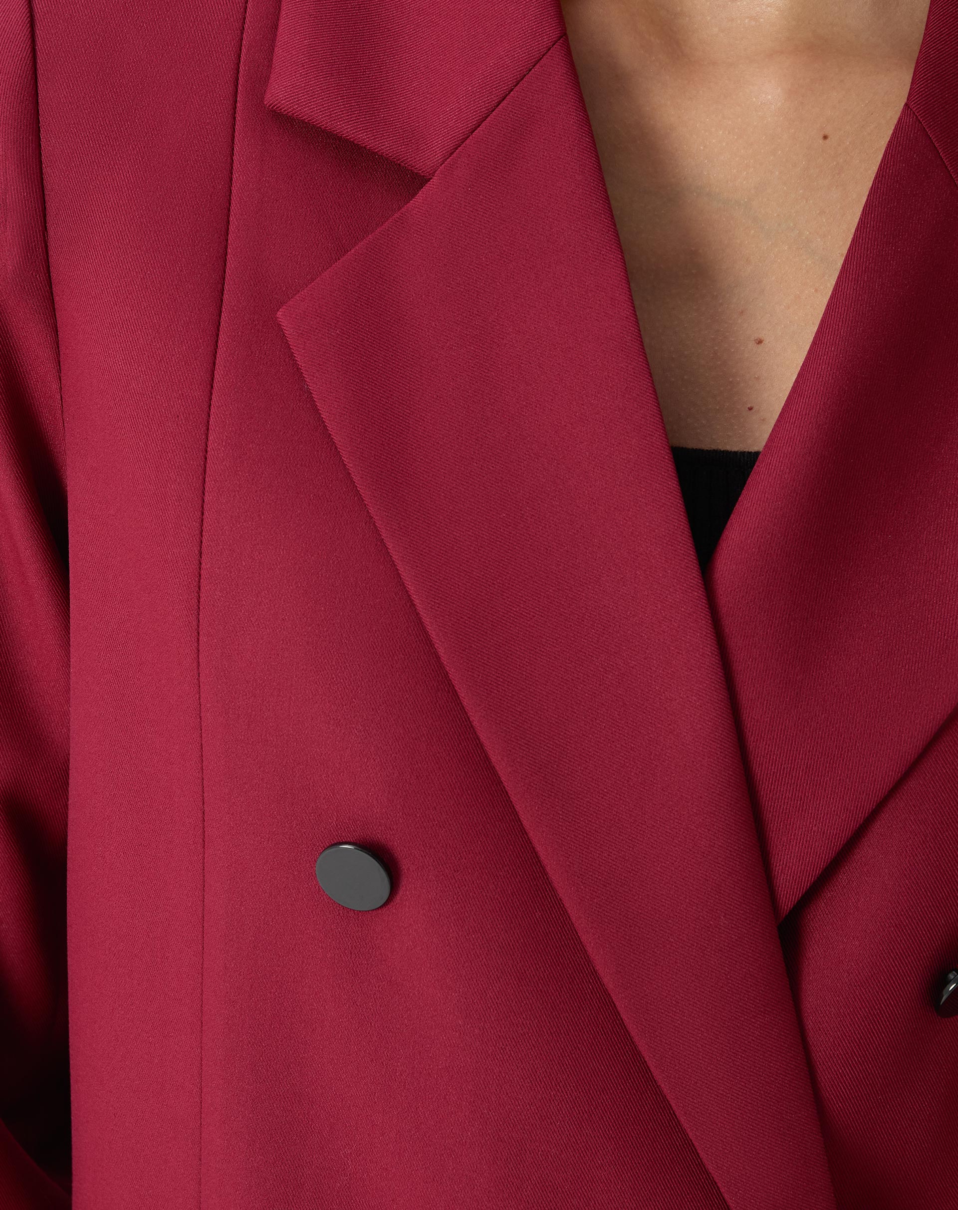 Detalhe frontal com as mãos da modelo nos bolsos embutidos do blazer vinho, mostrando o caimento solto.