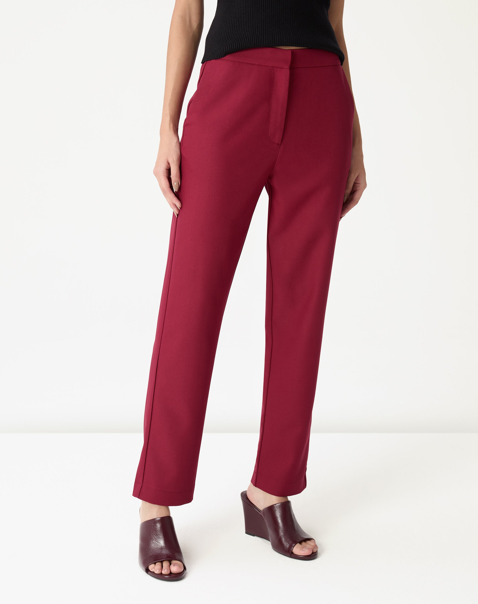 Detalhe frontal da calça alfaiataria vinho mostrando cós alto, pala frontal e bolso faca com acabamento liso