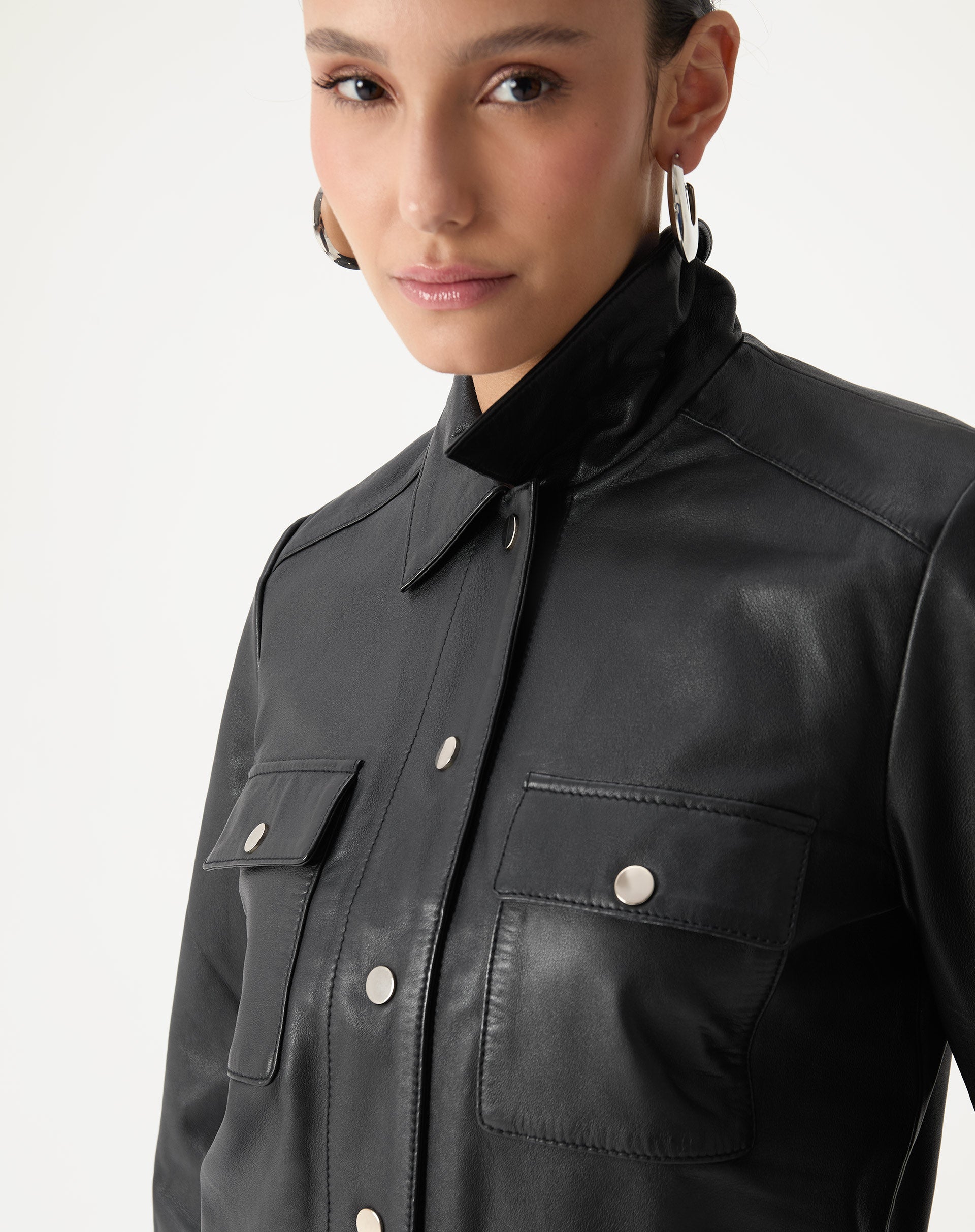 Detalhe do colarinho clássico e fechamento frontal por botões de pressão em jaqueta de couro preta, acabamento liso