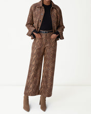 Look completo com jaqueta e calça combinando em estampa cobra caramelo, top preto e bota caramelo sobre fundo branco