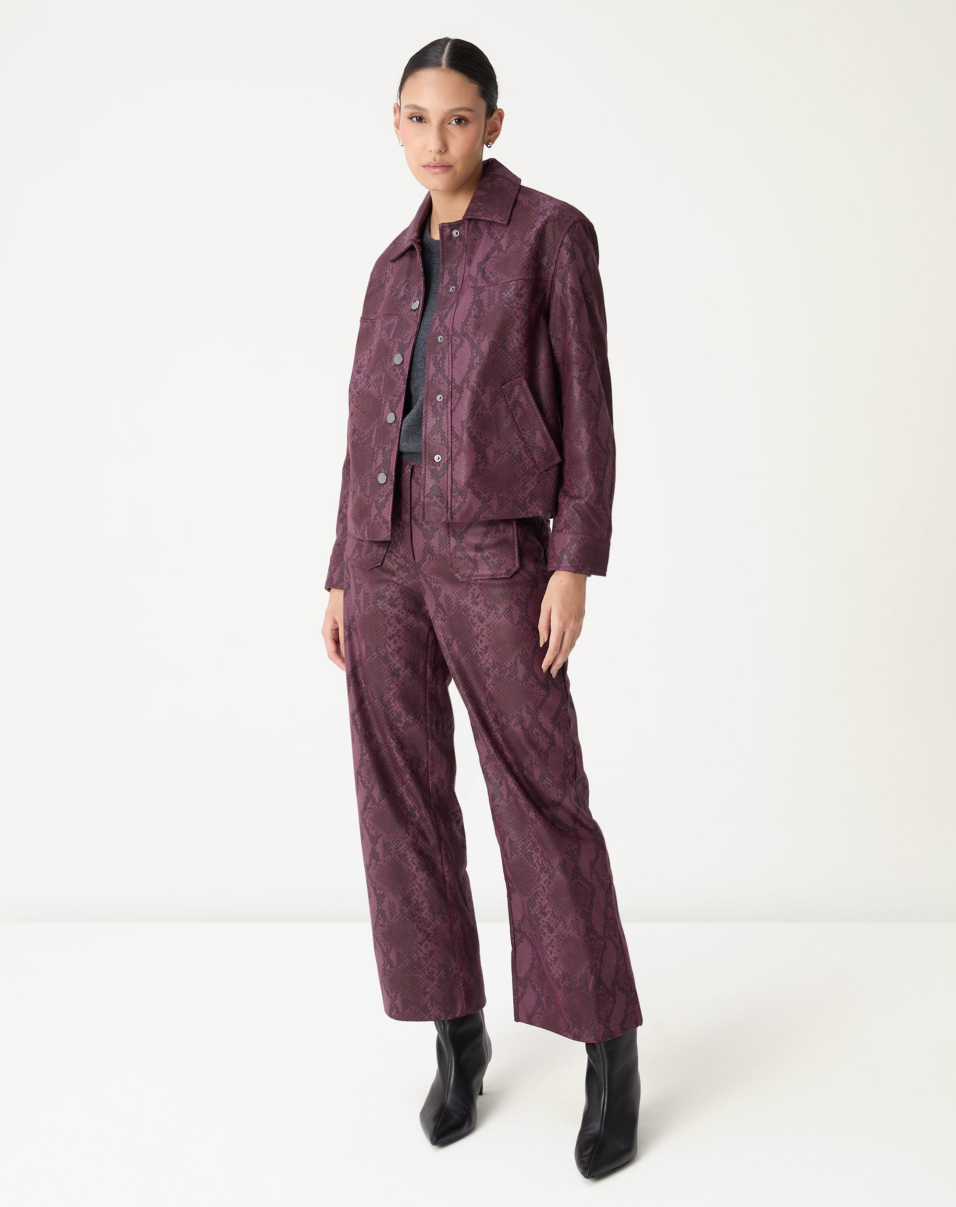 Detalhe frontal da jaqueta em PU vinho destacando a textura escamada, costuras horizontais no corpete e botão de metal.