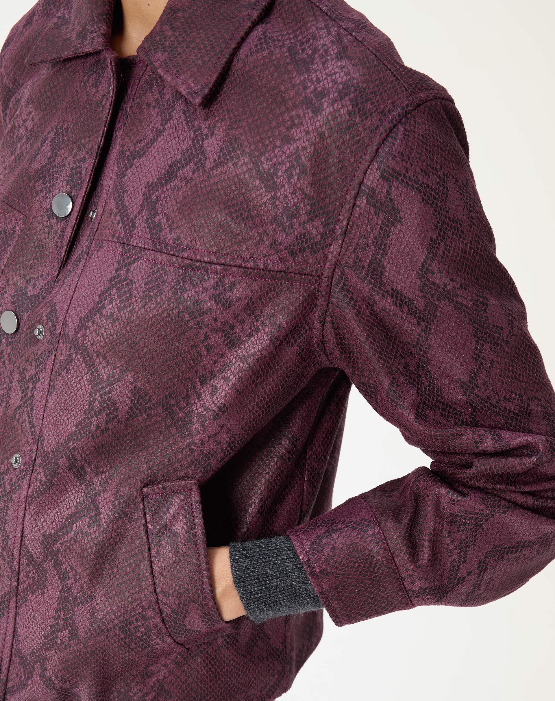 Enfoque no ombro e na manga da jaqueta cobra em PU vinho com costura estruturada e acabamento texturizado.