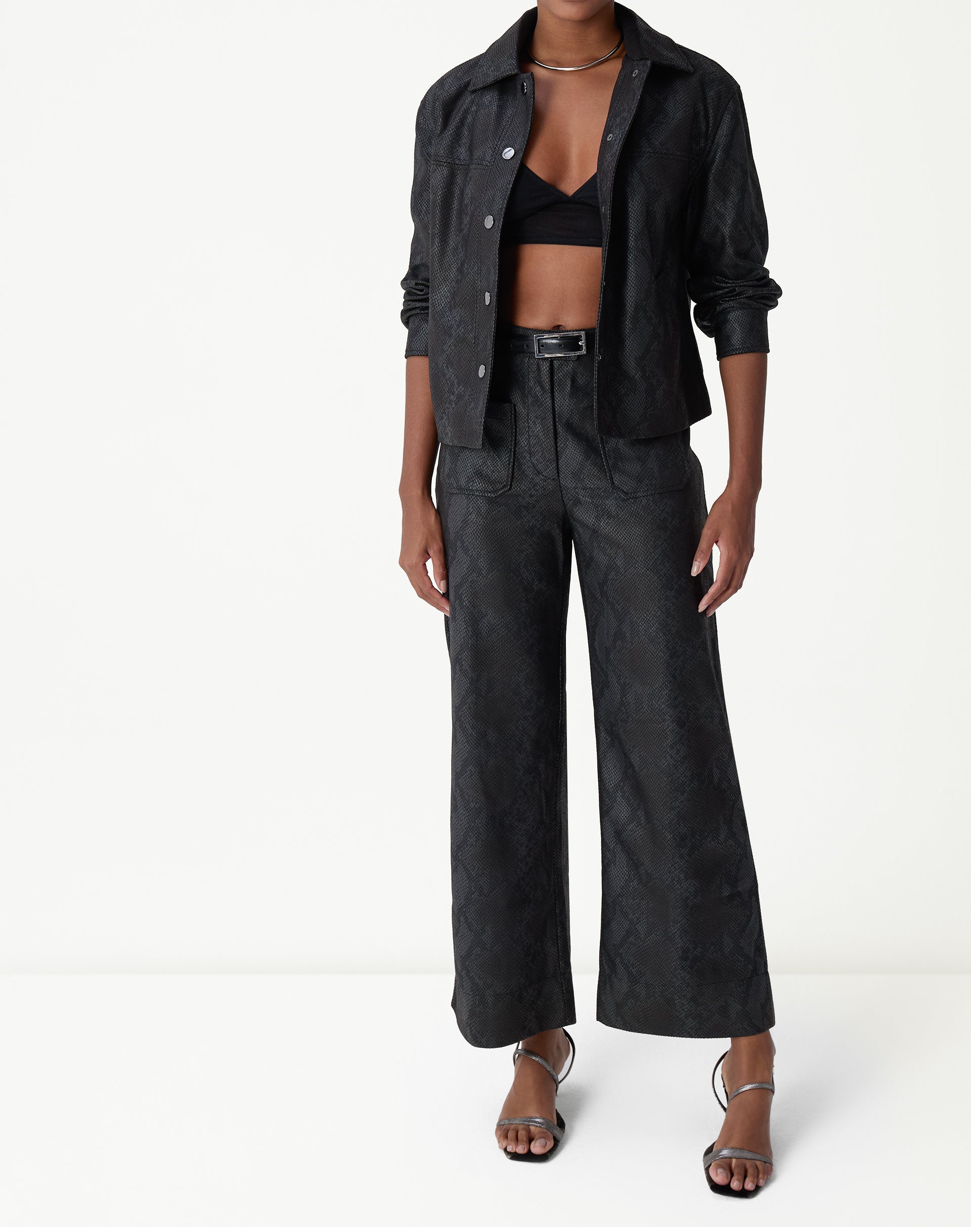 Calça reta cobra PU preta vista frontal em modelo com jaqueta combinando e top, cós alto e caimento reto