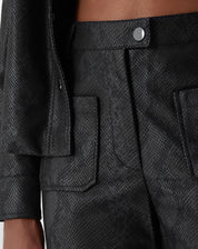 Vista traseira da calça cobra PU preta em modelo, mostrando linhas retas e barra com bainha aplicada