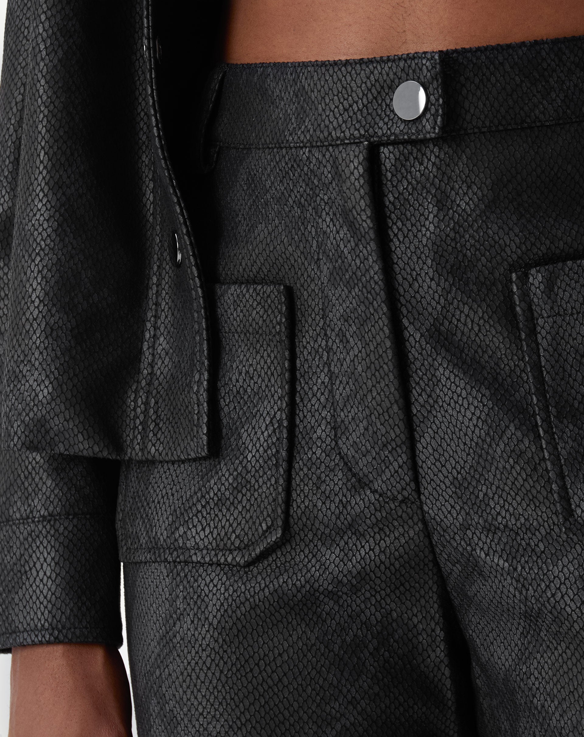 Vista traseira da calça cobra PU preta em modelo, mostrando linhas retas e barra com bainha aplicada