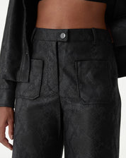 Calça cobra PU preta vista frontal em modelo em pé, destaque no cós alto e bolsos frontais aplicados