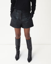 Close do cós e das pregas do shorts metalizado preto em suedine, mostrando passantes para cinto e acabamento das pregas