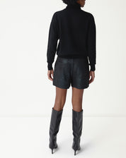 Vista de corpo inteiro frontal: shorts curto metalizado preto com suéter preto e botas de cano alto pretas, look moderno