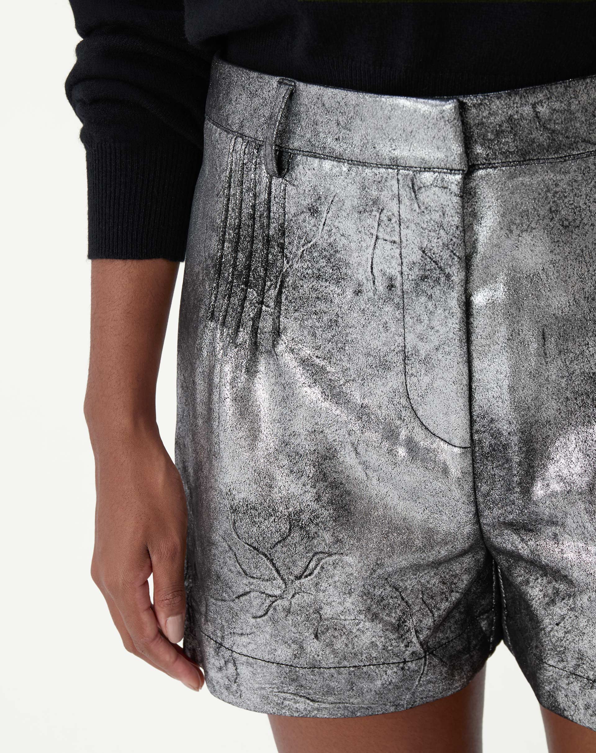 Close frontal do shorts metalizado prata mostrando pregas frontais, cós médio e bolso lateral em acabamento metalizado