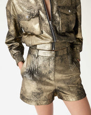 Detalhe frontal do shorts metálico dourado mostrando pregas, bolso embutido e textura suedine