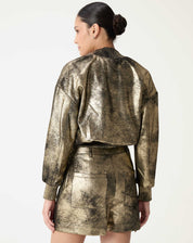 Verso do shorts metálico dourado em modelo, com bolsos traseiros e acabamento do cós