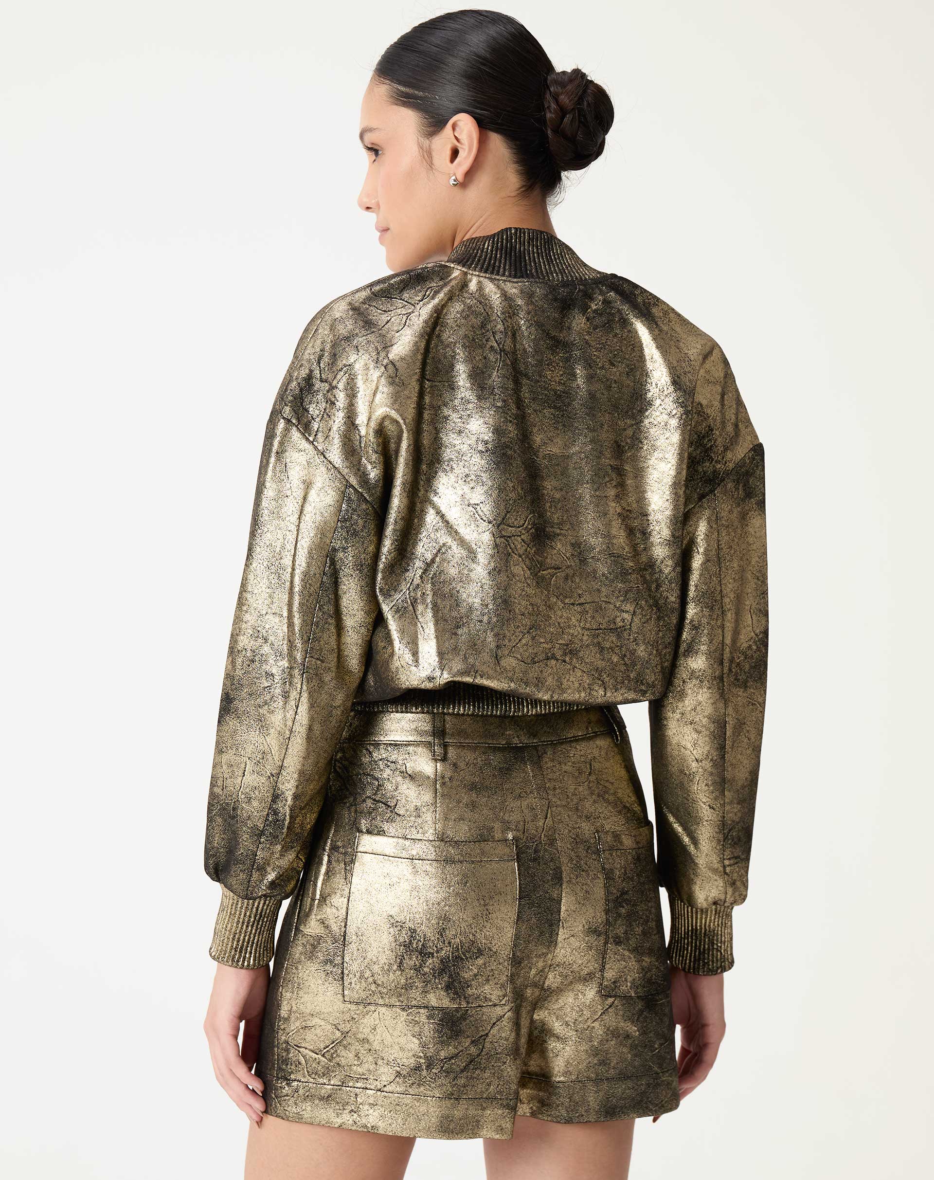 Verso do shorts metálico dourado em modelo, com bolsos traseiros e acabamento do cós