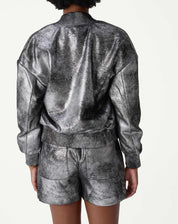 Detalhe em close dos bolsos de aba com botão da jaqueta bomber prata, textura metalizada desgastada e costuras visíveis