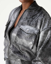 Close do torso mostrando zíper central e decote com top preto por baixo na jaqueta bomber prata, evidenciando acabamento metalizado