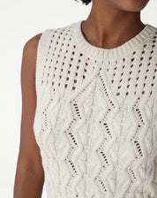 Detalhamento lateral da regata de tricô bege evidenciando decote redondo, cava e textura dos pontos abertos.