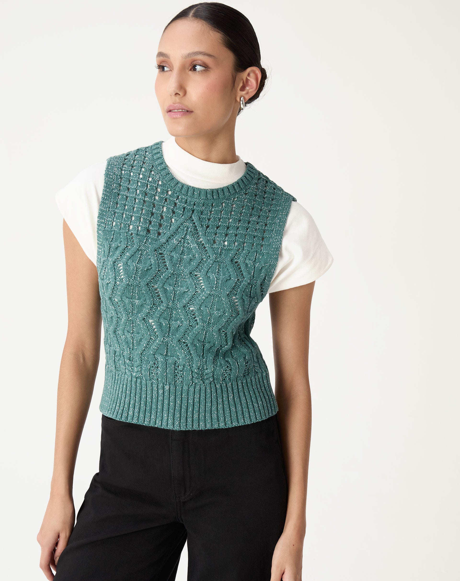 Modelo de pé usando regata tricot verde cropped sobre camiseta branca e calça preta, vista frontal mostrando decote redondo e barra canelada