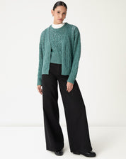 Look completo com regata tricot verde e cardigan tricot combinando, modelo em pé com calça pantalona preta, sugestão de sobreposição