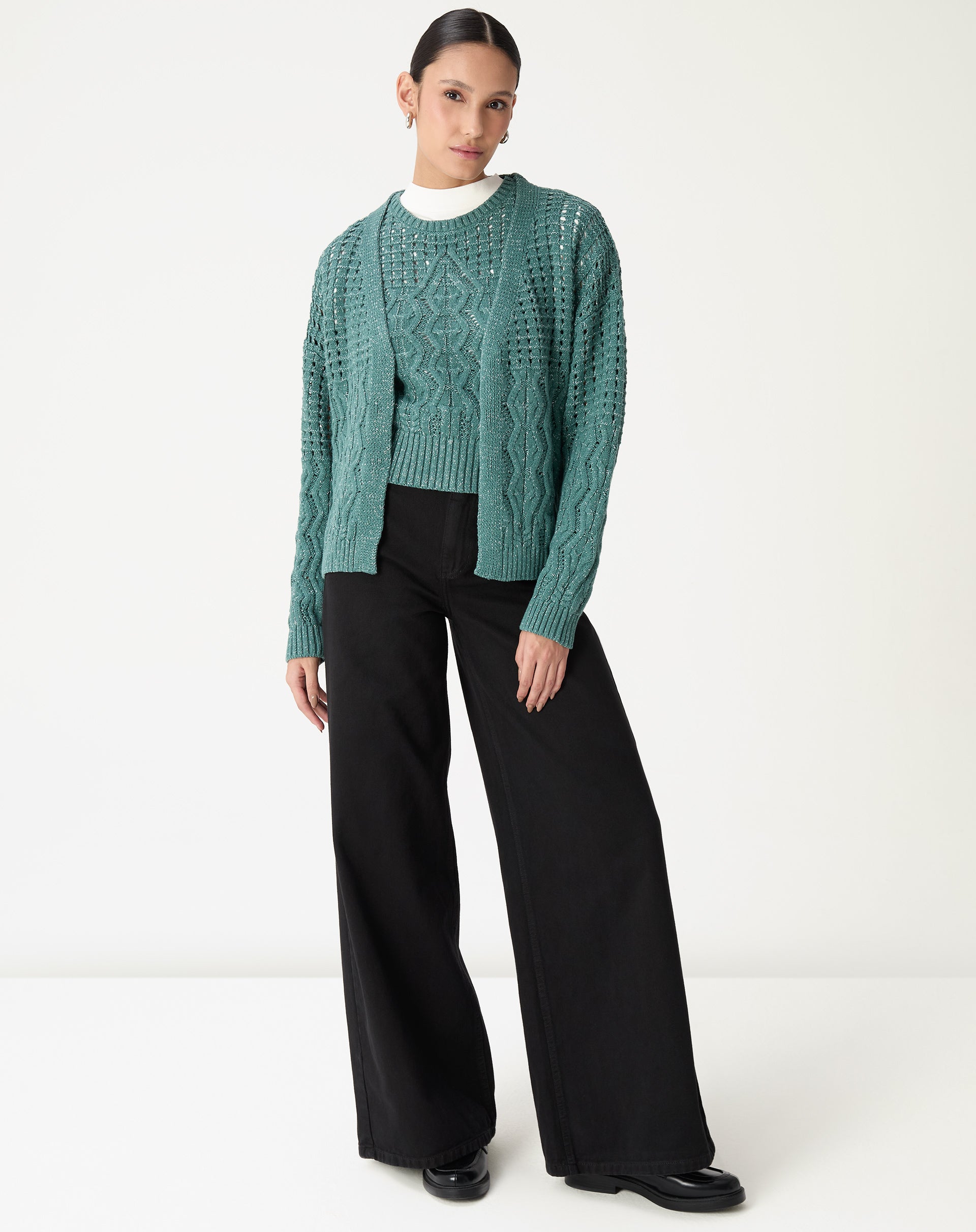 Look completo com regata tricot verde e cardigan tricot combinando, modelo em pé com calça pantalona preta, sugestão de sobreposição