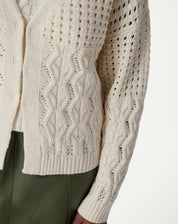 Detalhe frontal do cardigan de tricô bege mostrando ponto vazado, texturas verticais em tranças e barra canelada