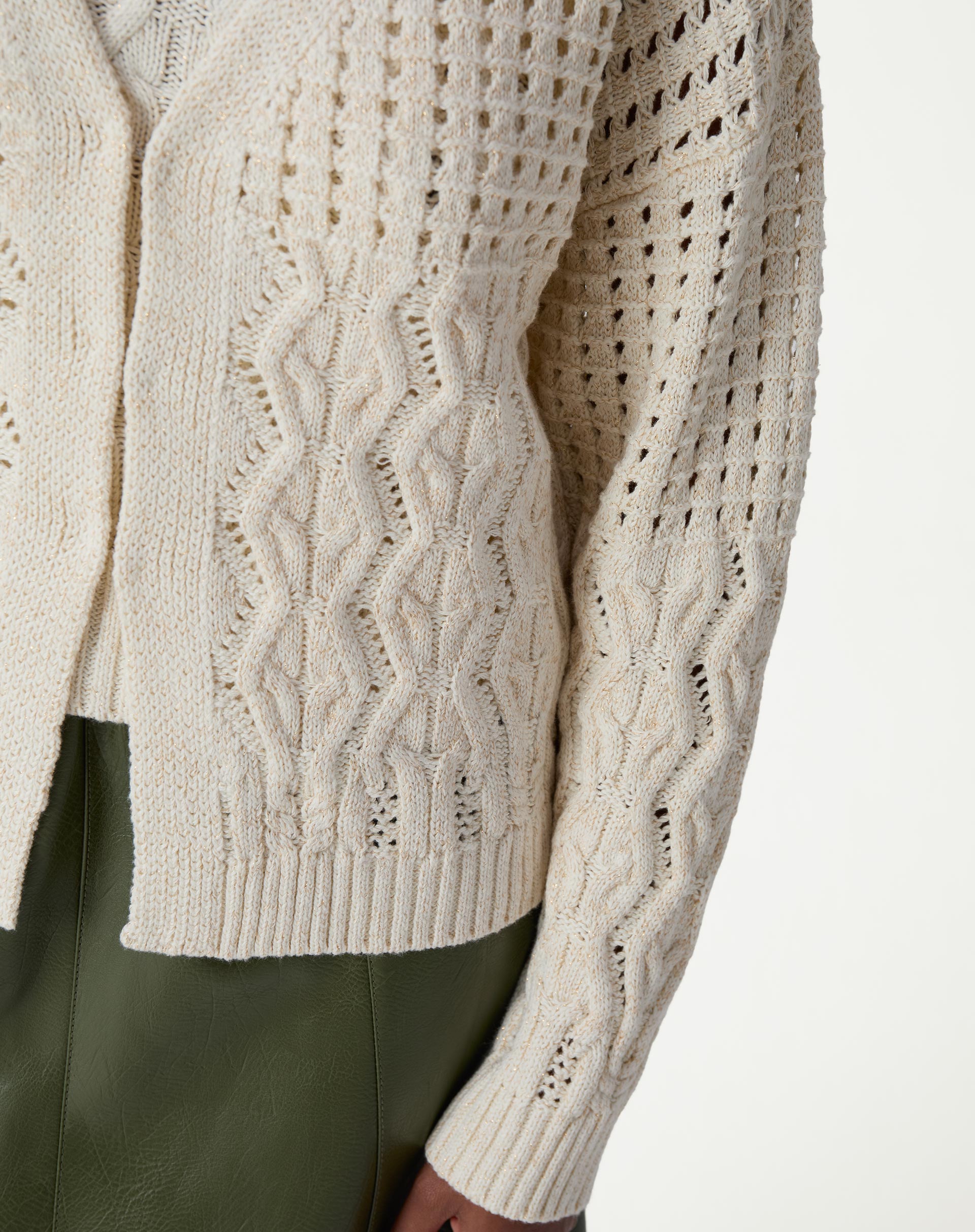 Detalhe frontal do cardigan de tricô bege mostrando ponto vazado, texturas verticais em tranças e barra canelada