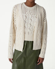 Modelo vestindo um cardigan de tricô bege com ponto diferenciado, visual de frente com saia midi verde - cardigan aberto e manga longa