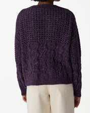 Look completo com modelo usando cardigan tricot roxo, calça wide-leg bege e sapato marrom, visual casual e sofisticado.
