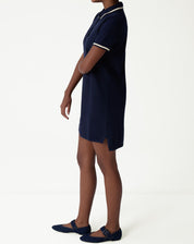 Side view of navy blue polo knit dress modeled, showing straight cut, small side slit and short length