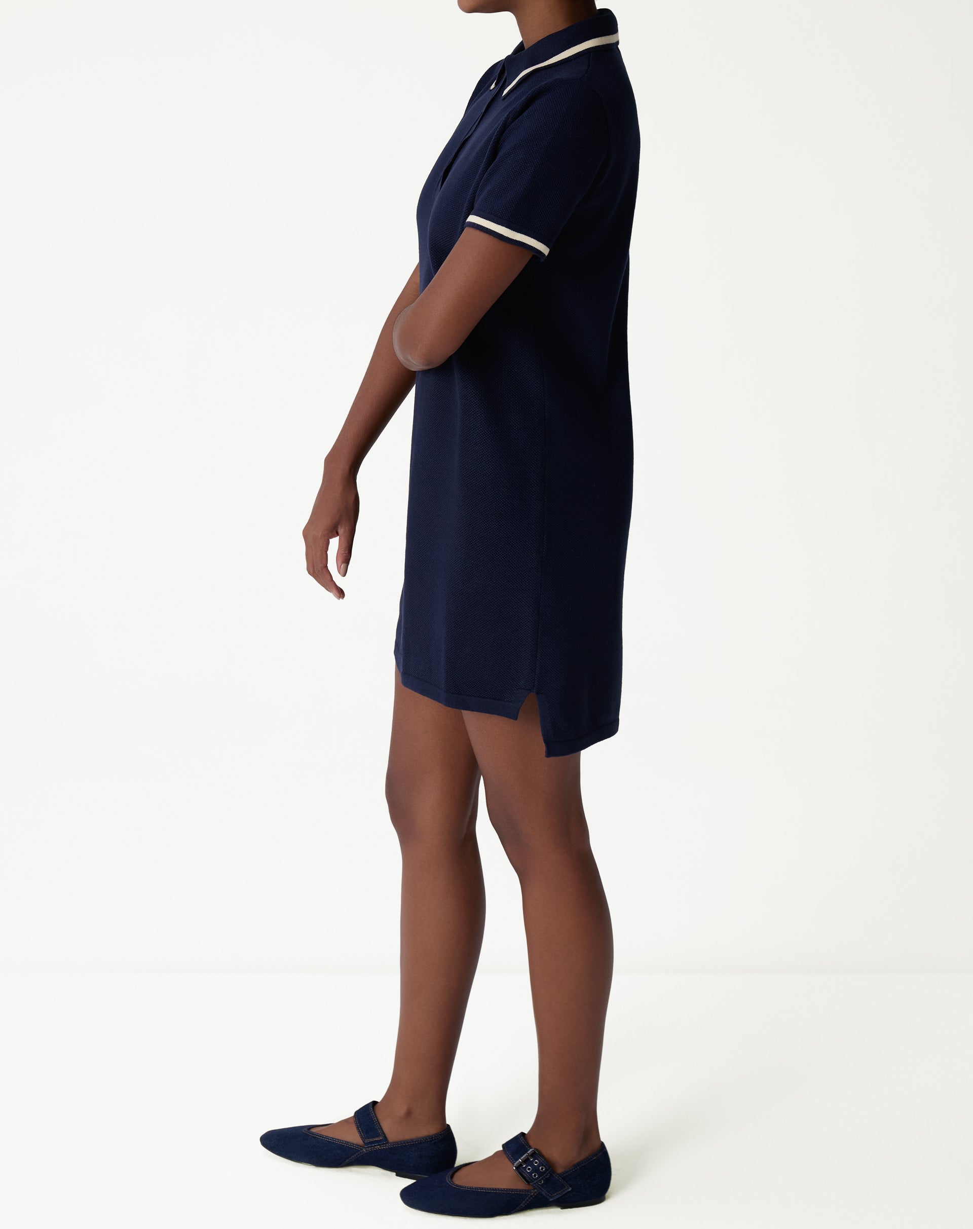 Side view of navy blue polo knit dress modeled, showing straight cut, small side slit and short length