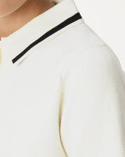 Vista lateral do vestido polo tricot off-white mostrando comprimento curto e pequena fenda lateral, caimento reto e manga curta