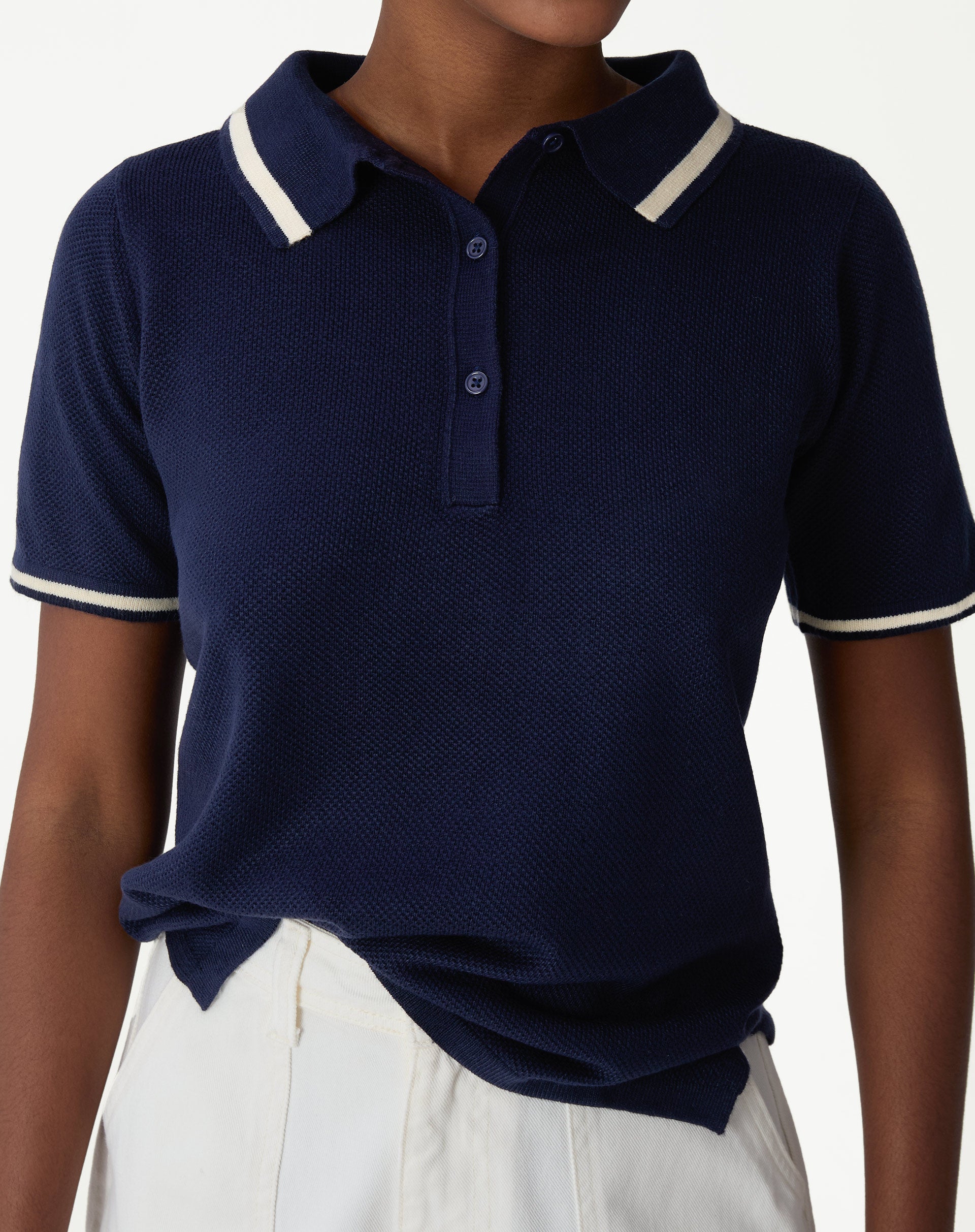 Close frontal da blusa polo tricot azul marinho mostrando a gola polo com paspas off-white, carcela de três botões e textura do tricot
