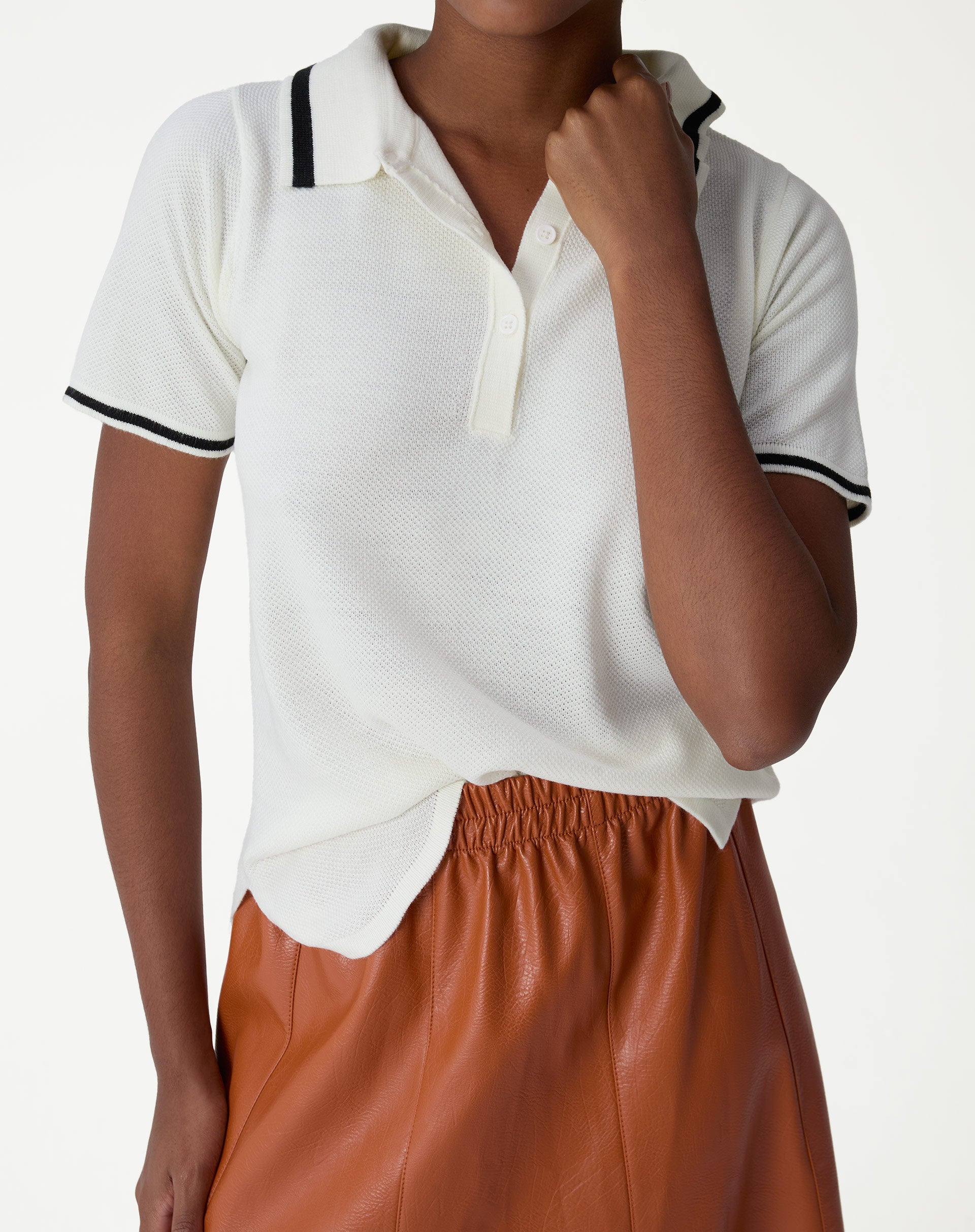 Blusa polo tricot off-white vista frontal em modelo com mão no decote, gola com filete preto, manga curta e textura piquê