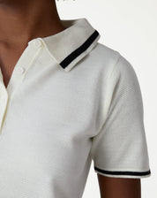 Modelo em pé usando blusa polo tricot off-white com jaqueta bomber preta e saia midi caramelo, look casual elegante