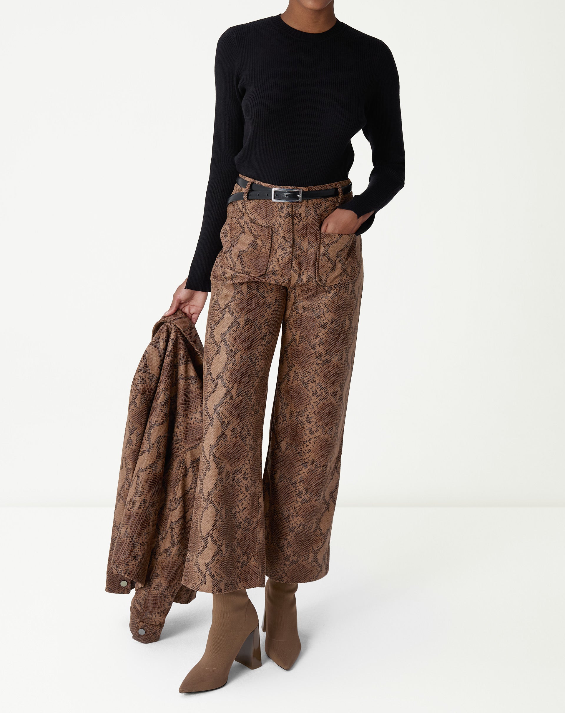 Fechamento do busto com braços cruzados mostrando o ajuste do suéter de tricô preto e o punho com fenda discreta.