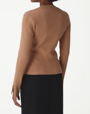 Primeiro plano da textura canelada do suéter de tricô bege, enfatizando o ajuste perfeito ao corpo e acabamento.